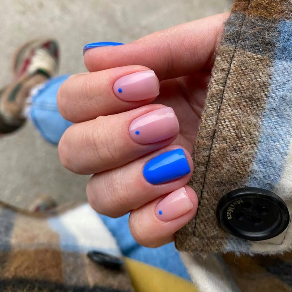 Short summer nails with pale pink base, cobalt blue accent nails and tiny blue dots on remaining nails