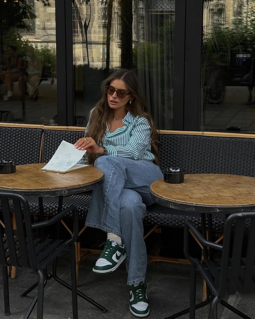 Casual summer outfit with green and white striped button-down shirt, relaxed fit medium blue jeans, brown sunglasses and green Nike sneakers
