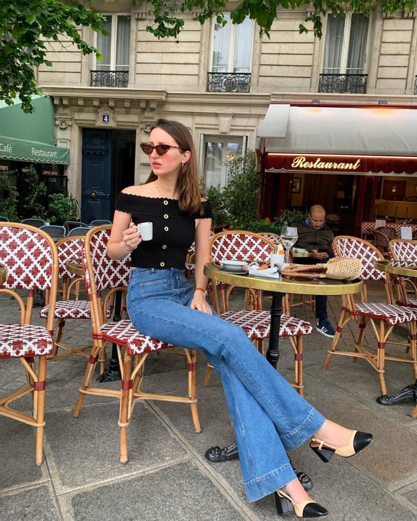 Parisian summer outfit with black ribbed off-shoulder buttoned top, medium wash flared jeans, tortoise sunglasses and two-tone slingback heels
