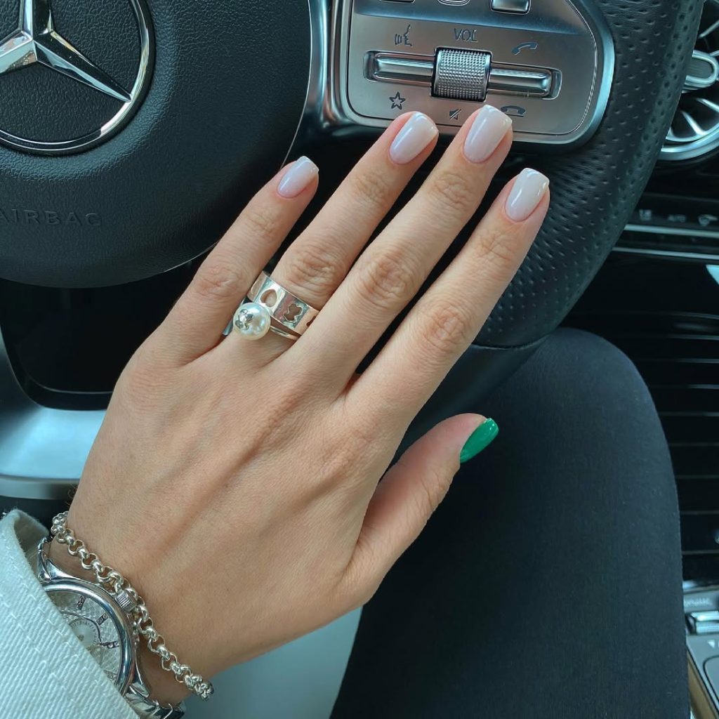 Short old money summer nails with opalescent milky white polish and one emerald green accent finger 