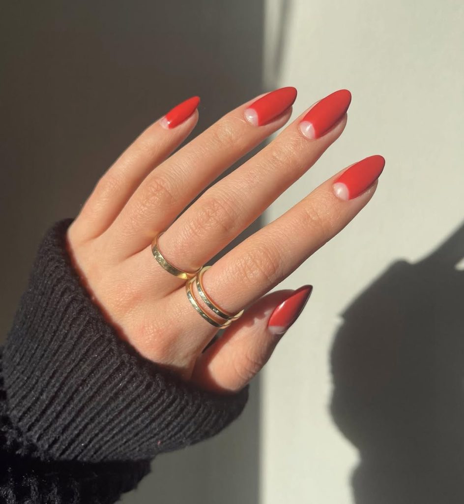 Almond shaped nails with coral-red polish and clear half-moon design at the cuticle area
