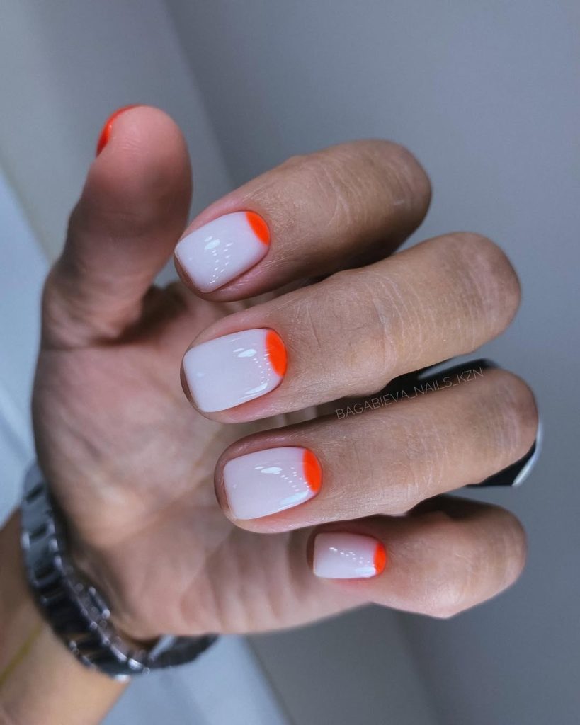 Short summer white nails with neon orange half moon design at cuticle