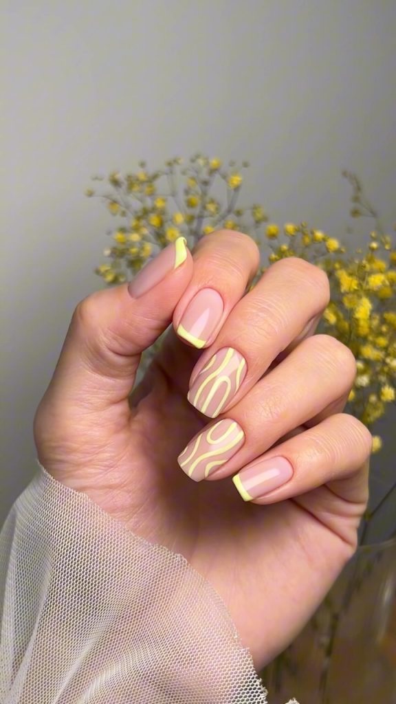 Classy June nails featuring square shape with nude base, pastel yellow French tips and abstract swirl pattern design