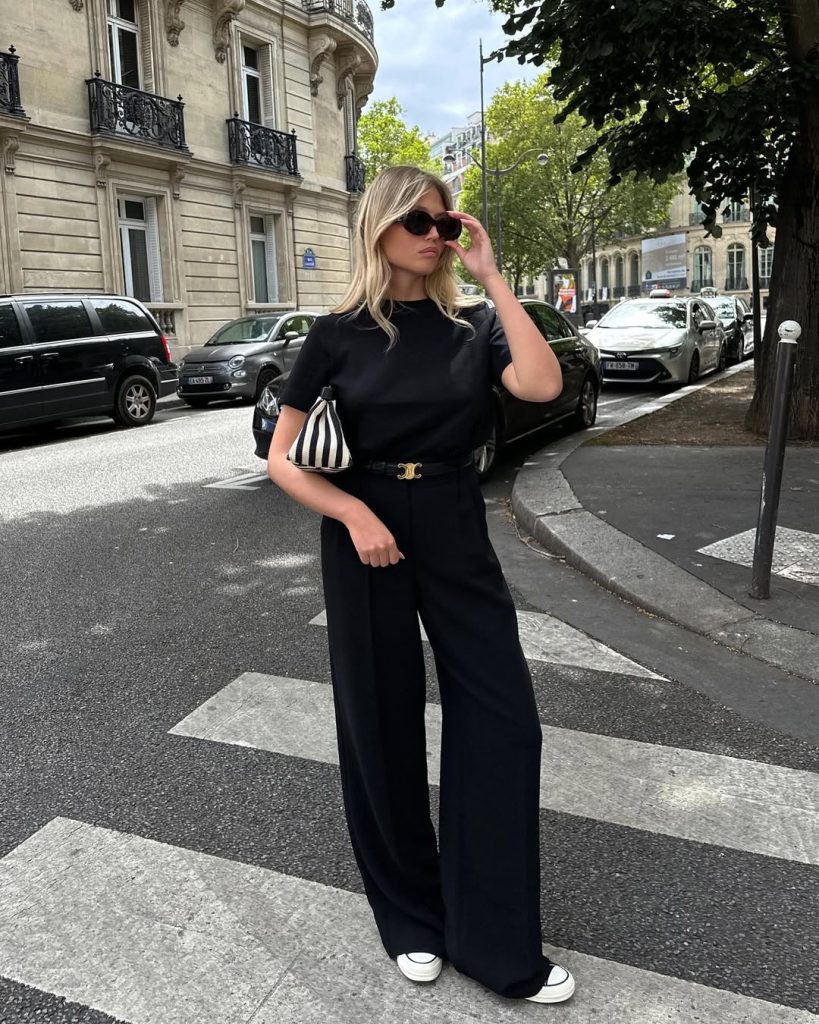 Summer outfit with black crewneck t-shirt, black wide-leg trousers, gold logo belt, white sneakers and black and white striped shoulder bag
