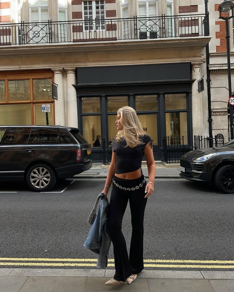 Night out outfit with black fitted crop top, black flare pants with silver chain belt, beige pointed flats and denim jacket
