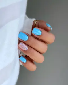 Short July nails with bright sky blue polish and one accent nail with gold lines and small blue flower details
