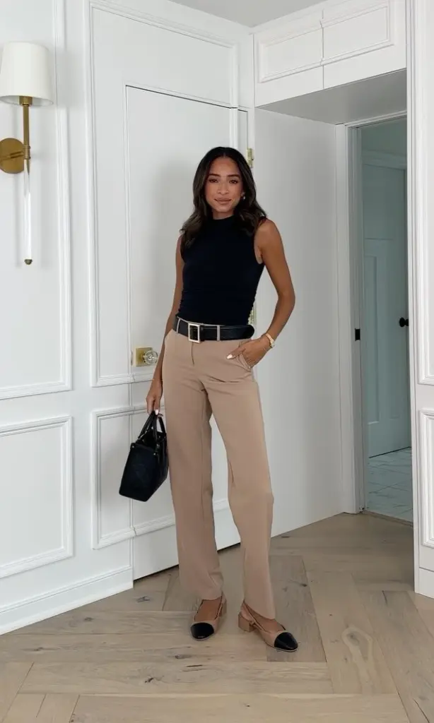 summer work outfit with black sleeveless mock neck top, beige straight-leg trousers, wide black belt, black tote bag and two-tone beige flats

