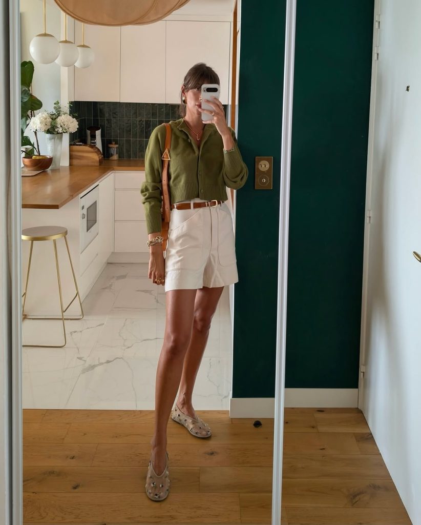 Summer outfit with olive green cropped knit top, white tailored shorts, brown leather belt, beige studded loafers and tan leather shoulder bag