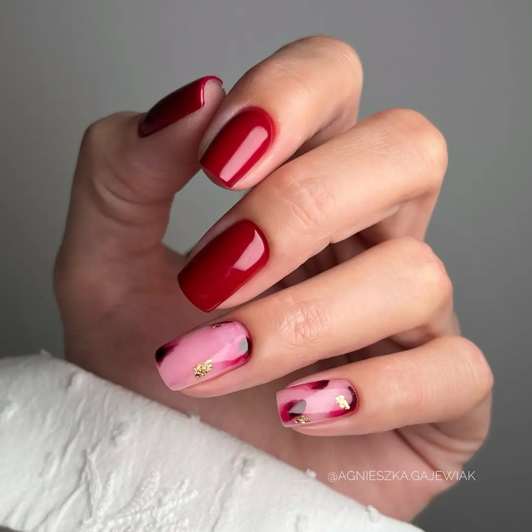 Short square nails with glossy burgundy red polish and pink accent nails with red watercolor effect and gold foil accents