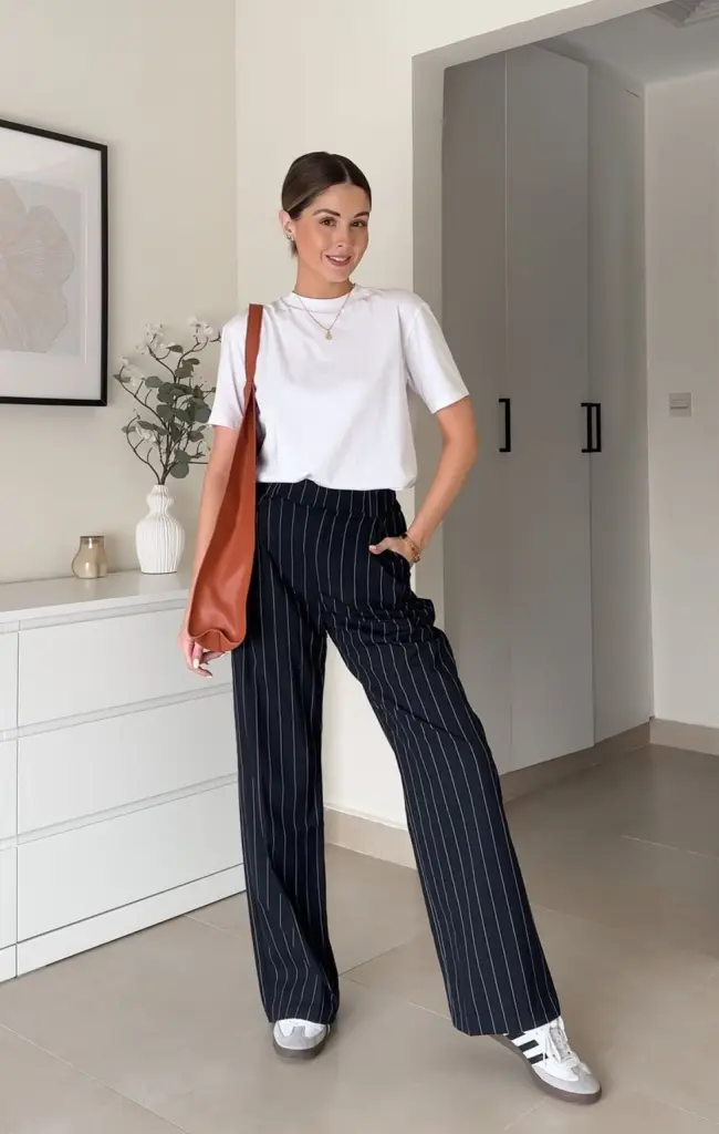 ummer work outfit with white crewneck t-shirt, navy pinstriped wide-leg trousers, cognac leather tote bag and silver athletic sneakers
