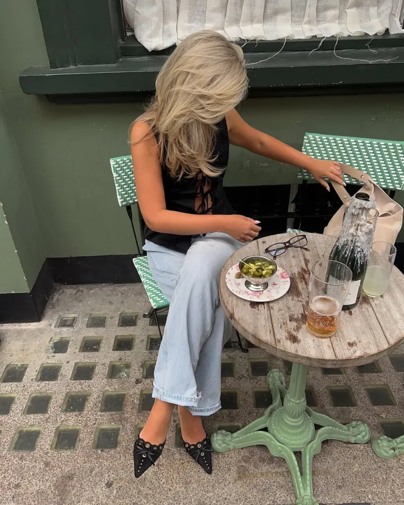 Casual summer date night outfit with black tie-back sleeveless top, light-wash wide-leg jeans, black pointed studded heels and cream leather tote 