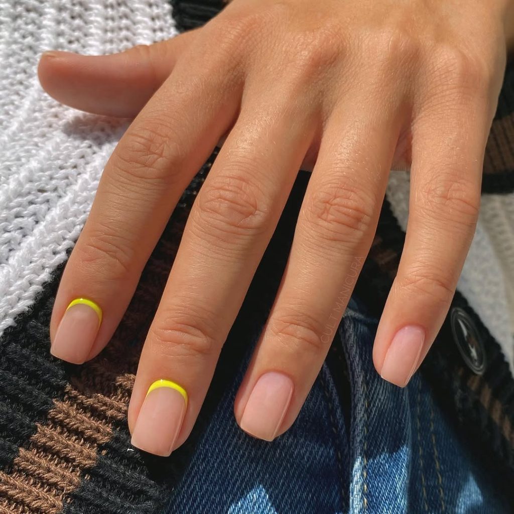 Short summer nails with glossy nude polish and bright yellow cuticle line accents