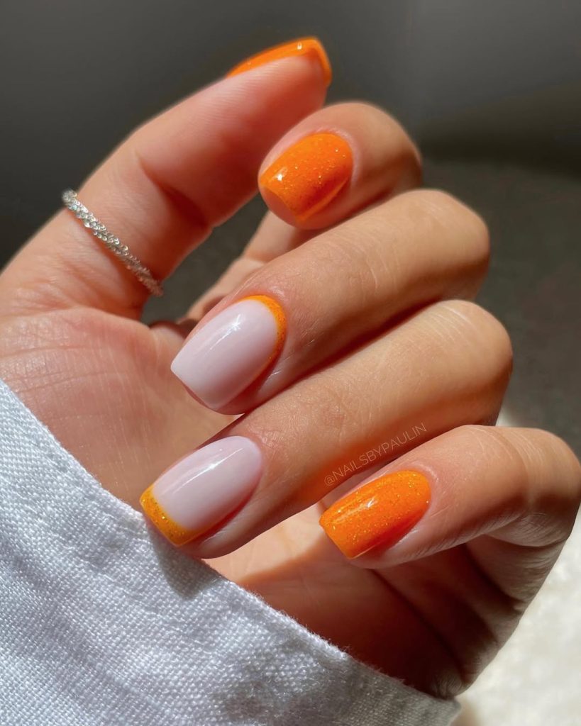Short nails with shimmery neon orange and milky base with orange French tips
