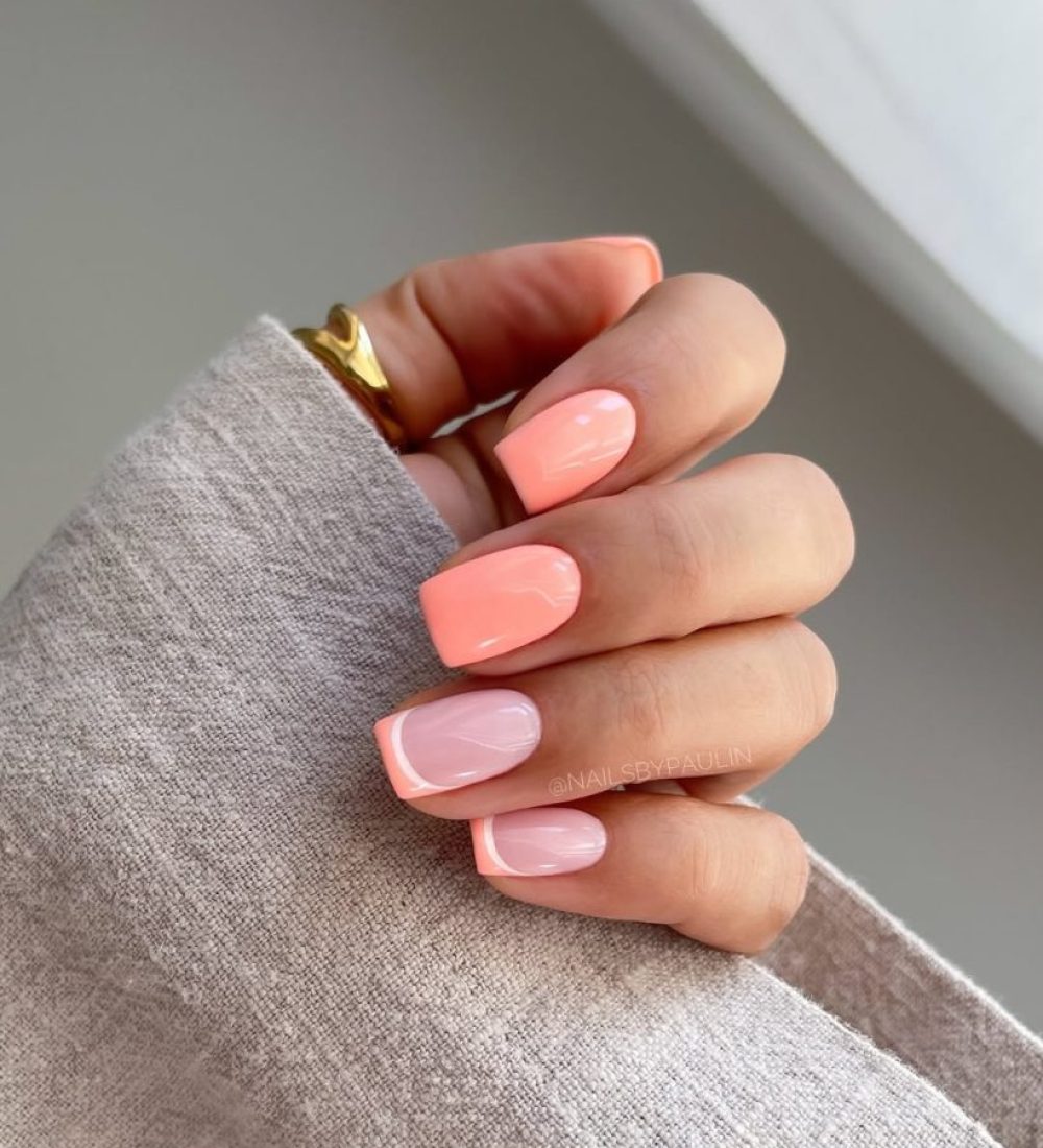 Short summer nails alternating between full coral polish and pale pink nails with coral French tips