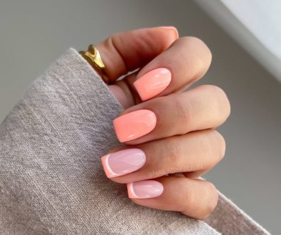 Short summer nails alternating between full coral polish and pale pink nails with coral French tips
