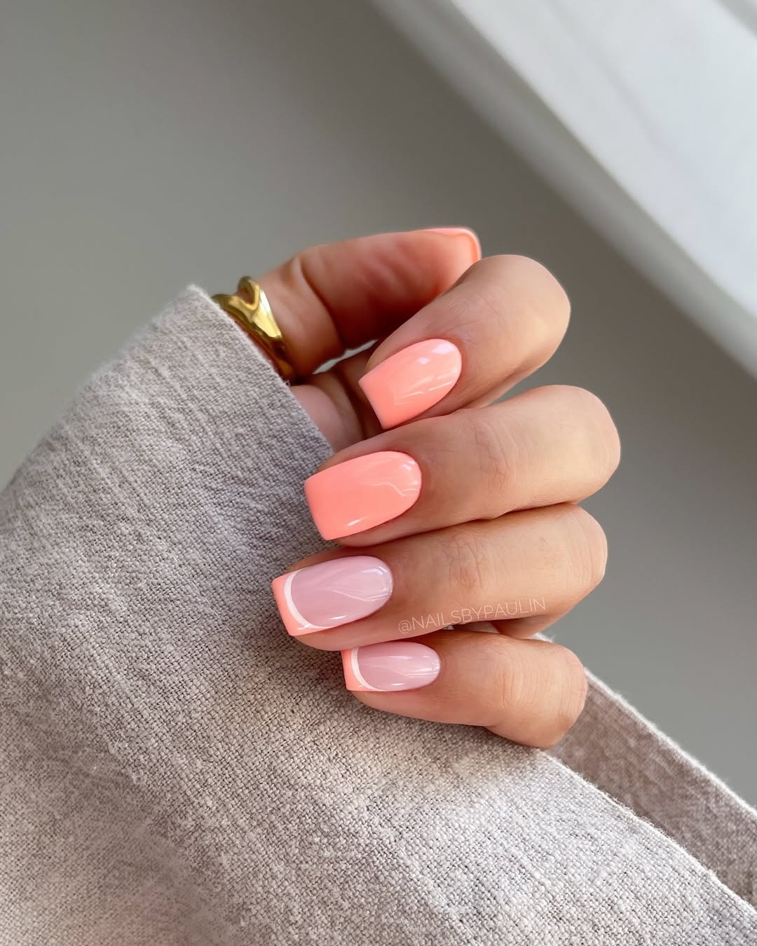 Short summer nails alternating between full coral polish and pale pink nails with coral French tips