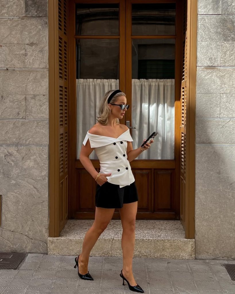 Old money summer outfit with white off-shoulder double-breasted top, black tailored shorts, black slingback heels, velvet headband and thin gold bracelets