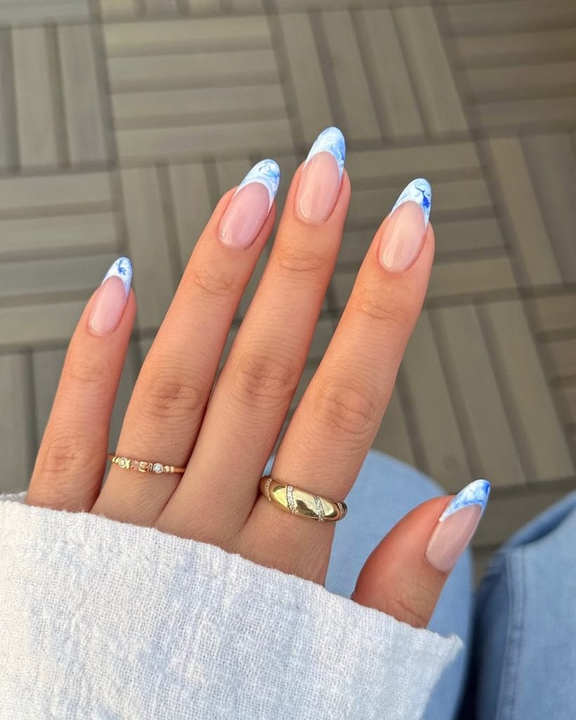 Long oval vacation nails with nude base and blue cloud French tip design
