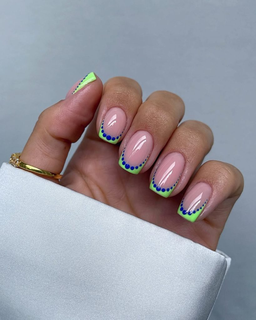 Short square nails with pink base, neon lime French tips and blue dot details
