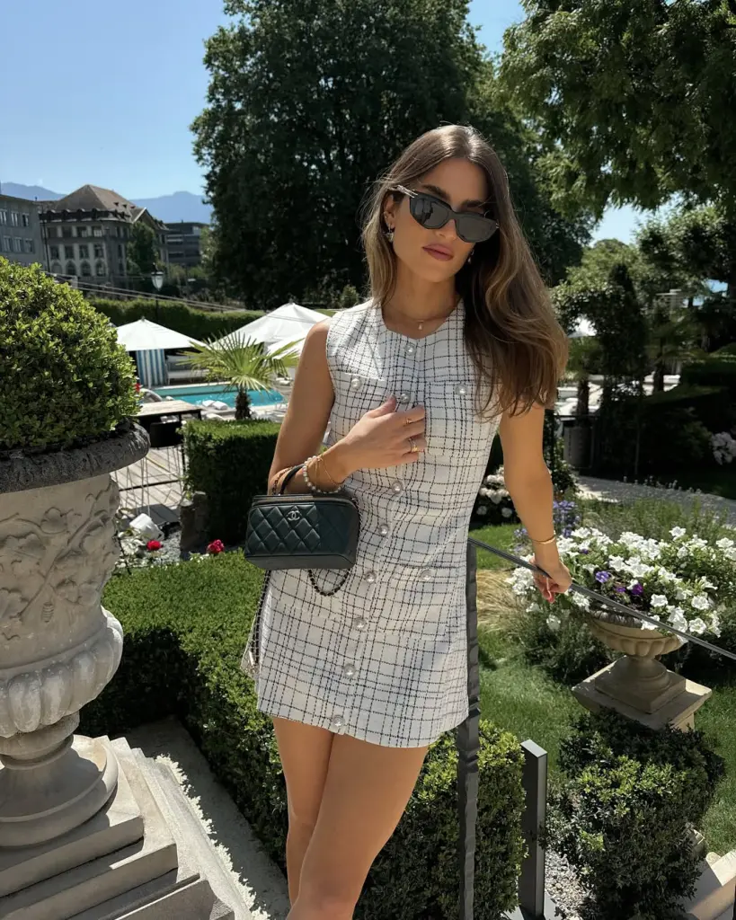 Current image: Old money summer outfit with white and black checked sleeveless mini dress, black quilted designer handbag, and black pointed heels