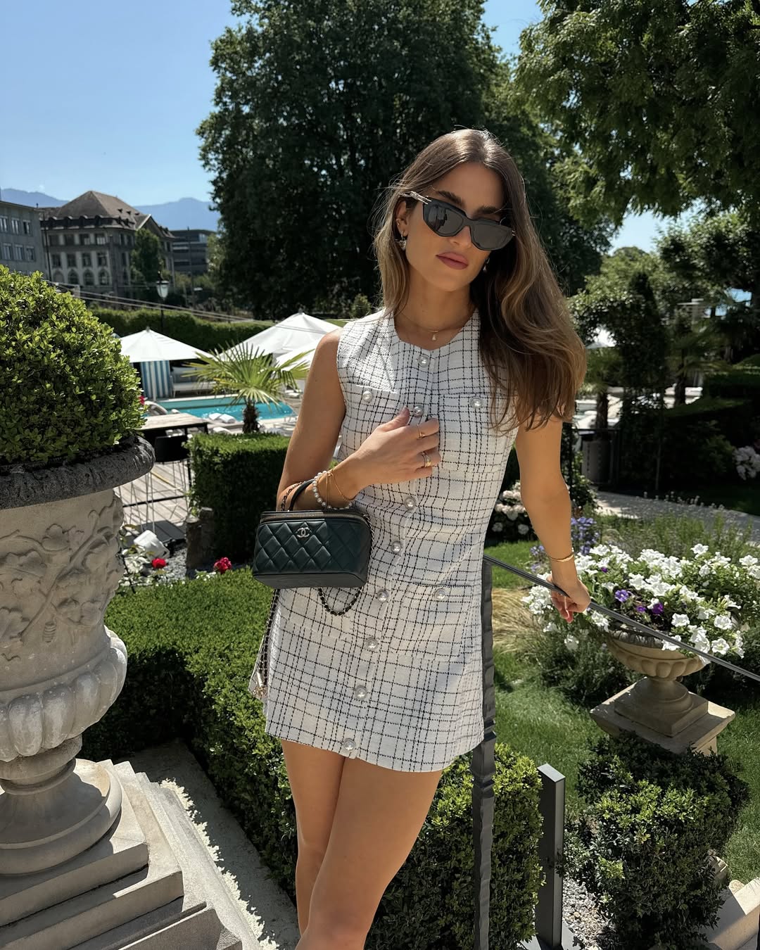 Old money summer outfit with white and black checked sleeveless mini dress, black quilted designer handbag, and black pointed heels