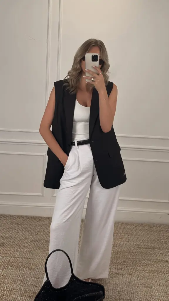 Sophisticated summer work outfit with black longline vest, white tank top, white tailored linen trousers and thin black belt