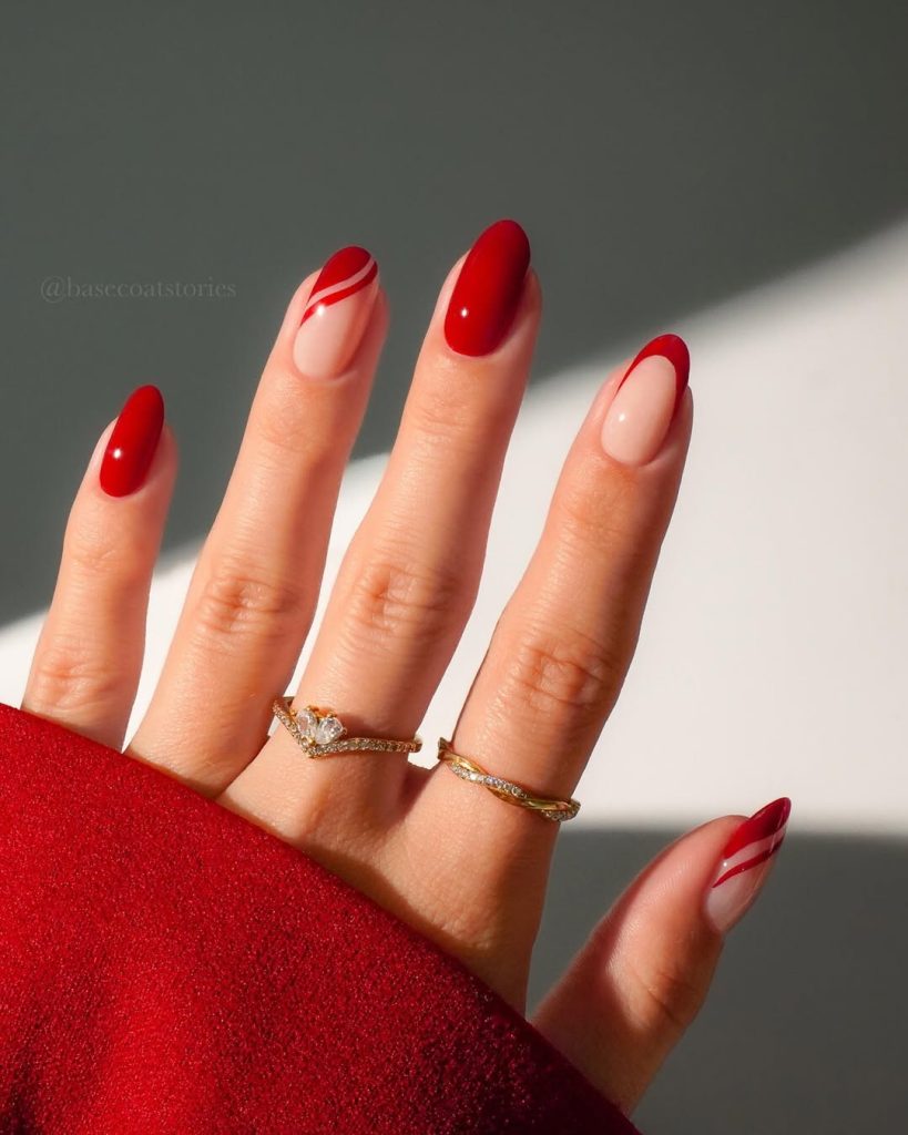 Almond shaped nails with alternating solid red and sheer base with curved red line designs and french tips