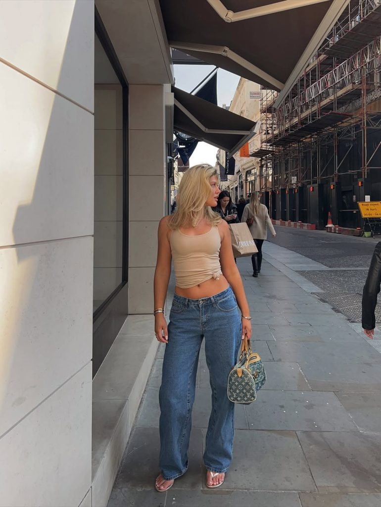 Casual summer outfit with cropped beige ribbed tank top, medium blue wide-leg jeans, minimalist silver jewelry and designer mini duffel bag