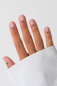 classy short summer nails with transparent pink polish featuring gold-rimmed blue evil eye charms