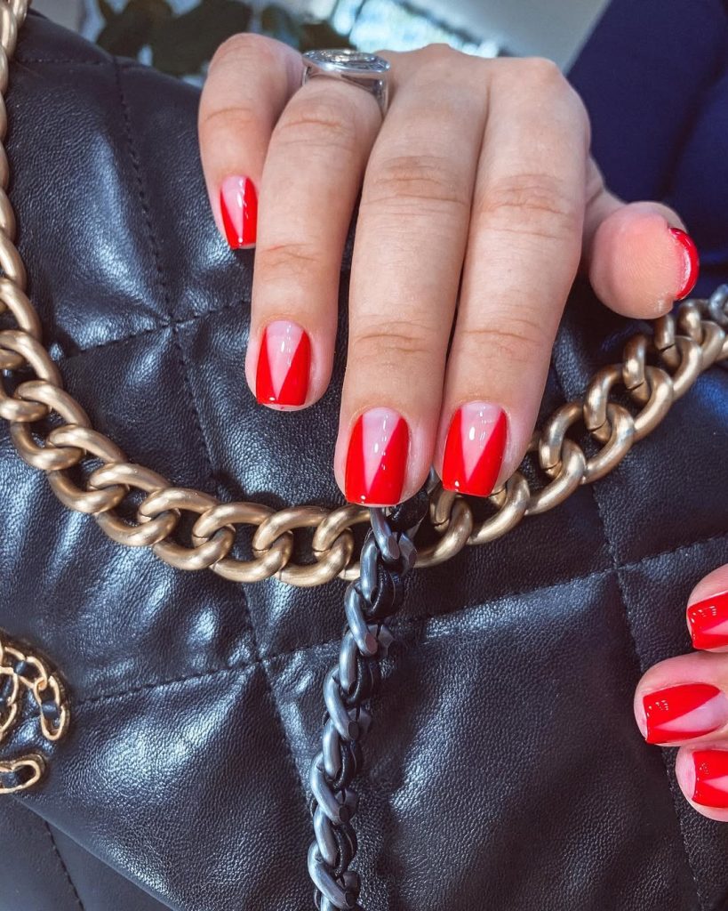Short square nails with negative space design featuring red V-shapes on nude base