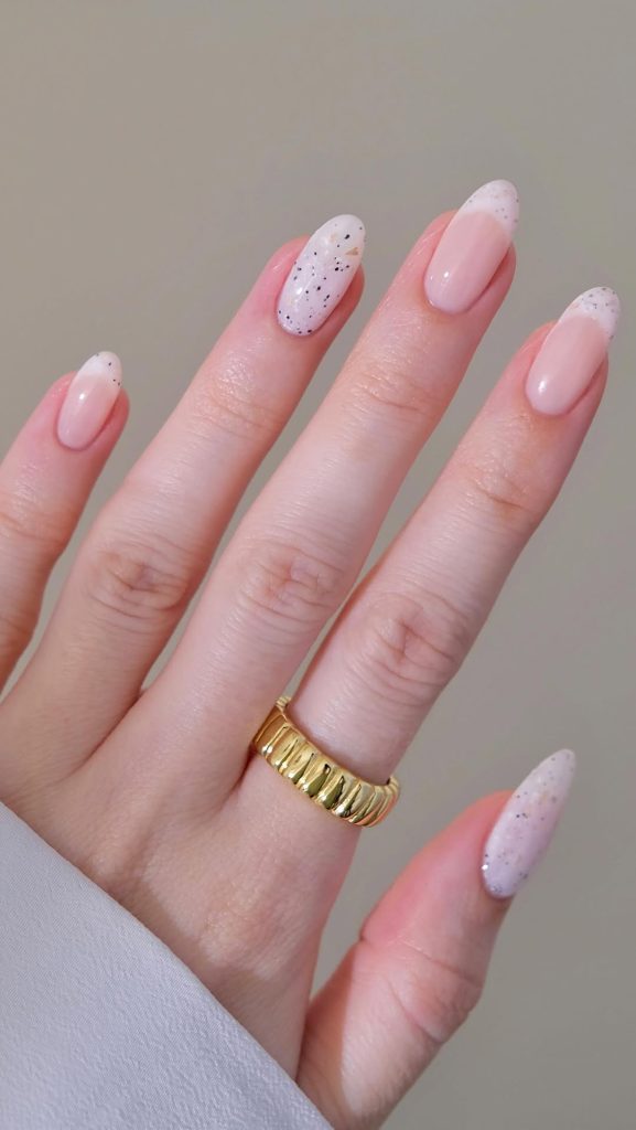 Almond shaped summer nails with milky white base, black speckled accent nails and subtle French tips