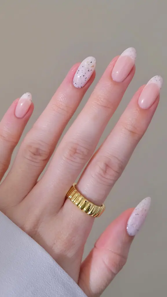 Almond shaped summer nails with milky white base, black speckled accent nails and subtle French tips 