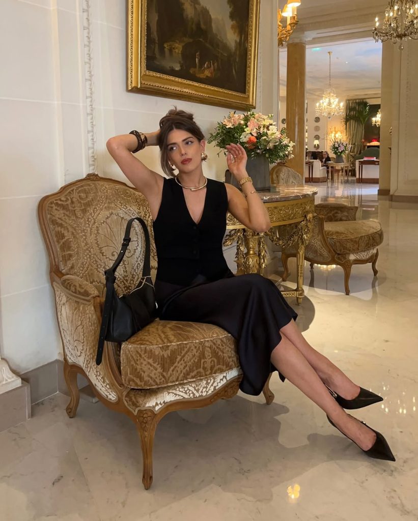 Elegant old money summer outfit with black sleeveless button-front vest, matching black midi skirt, silver choker necklace, statement earrings and leather shoulder bag