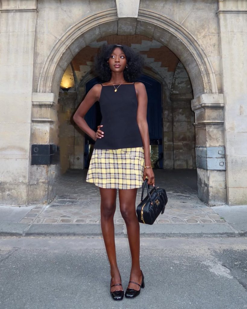 Summer outfit with black square-neck tank top, yellow plaid mini skirt, black patent mary janes and black structured handbag
