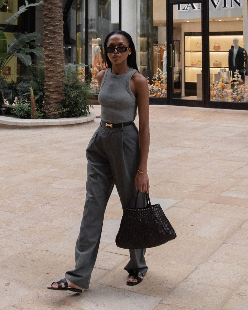 Old money summer outfit with grey fitted tank top, matching grey wide-leg trousers, designer gold belt, black woven tote bag and black flat sandals