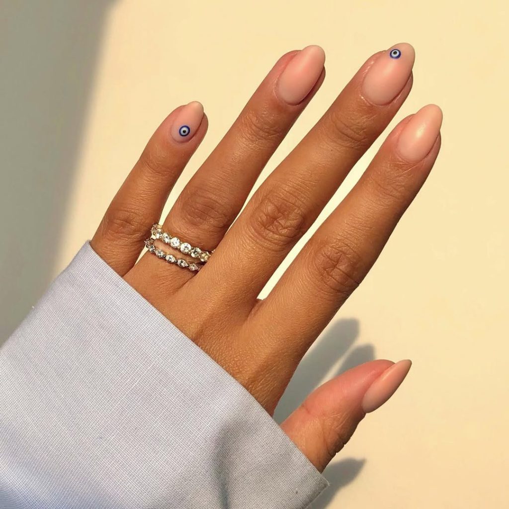 old money nude nails with minimalist blue evil eye designs on accent fingers