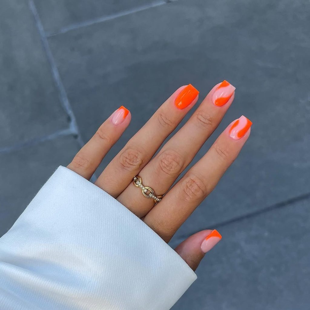 Square nails with nude base and vibrant orange swirl designs creating a bold summer manicure look