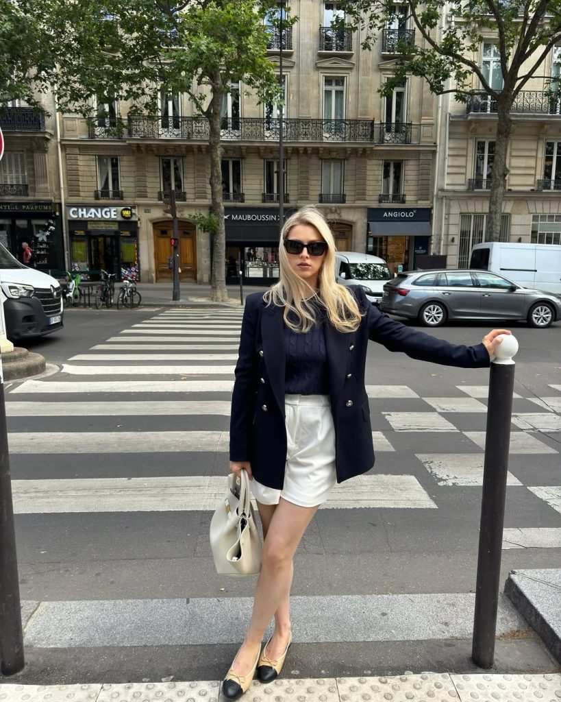 Summer outfit with navy double-breasted blazer, navy top, white tailored shorts, cream and black cap-toe flats and structured cream bag