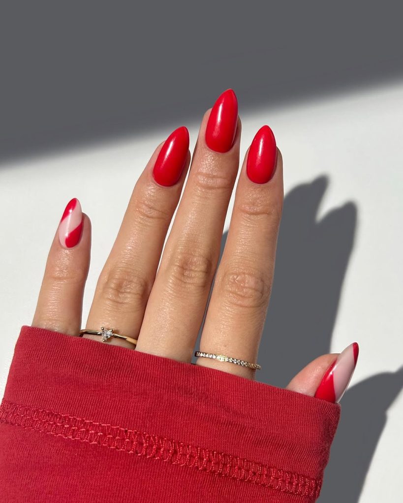 Almond shaped nails with solid red polish and accent clear nails featuring diagonal red details