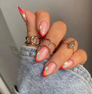 Long almond July nails with nude base and colorful rainbow French tips in red orange yellow and blue
