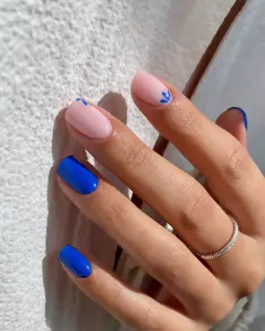 Short July nails with milky base, bright blue accent nails, and small blue flower designs