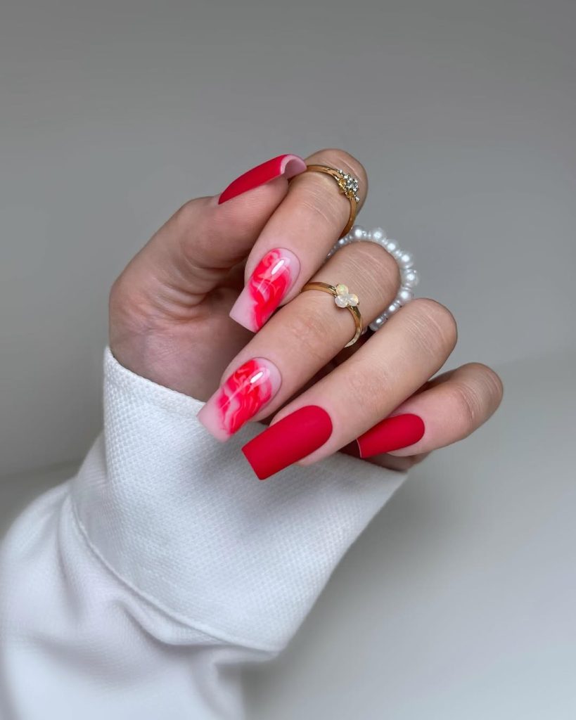 Long square nails with mix of solid matte red nails and nude base with glossy red marble design