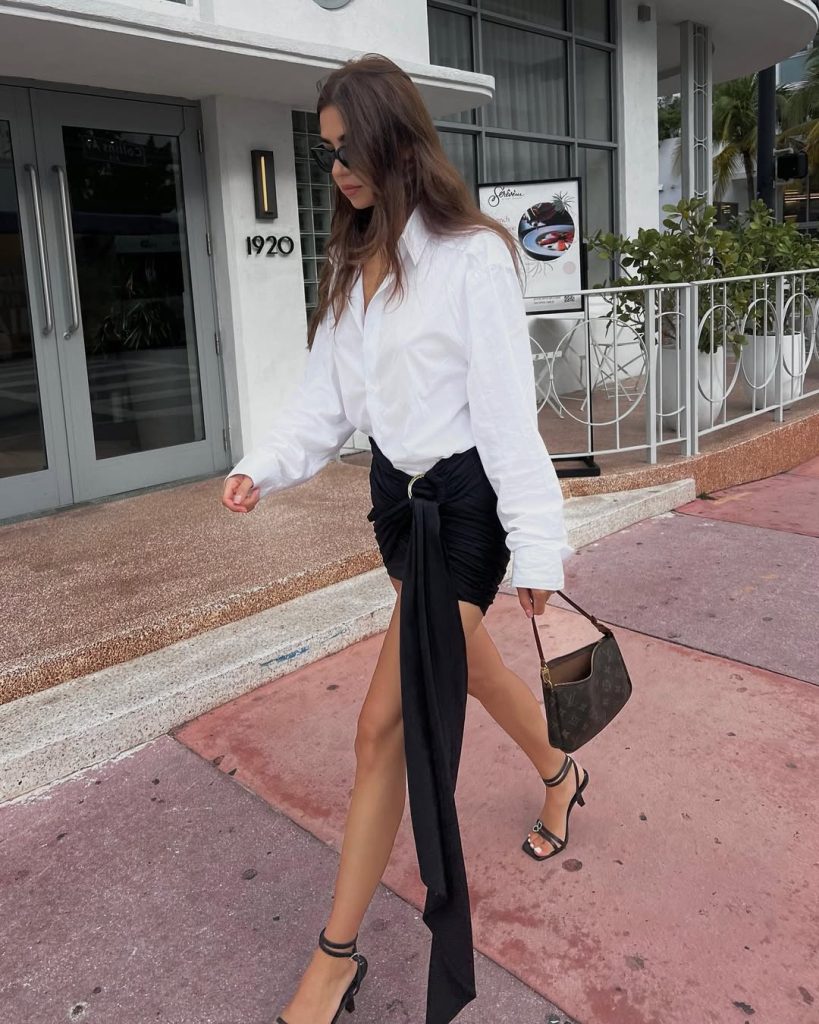 Night out outfit with crisp white button-down shirt, black draped mini skirt with dramatic side panel, slim sunglasses and black strappy heels
