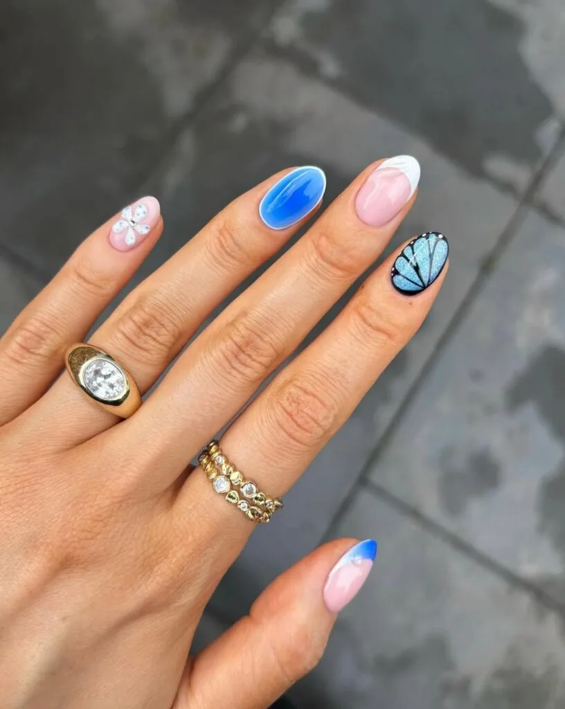 short summer nails, mixed blue set with butterfly wing art, halo accent, crystal flower, and French tip
