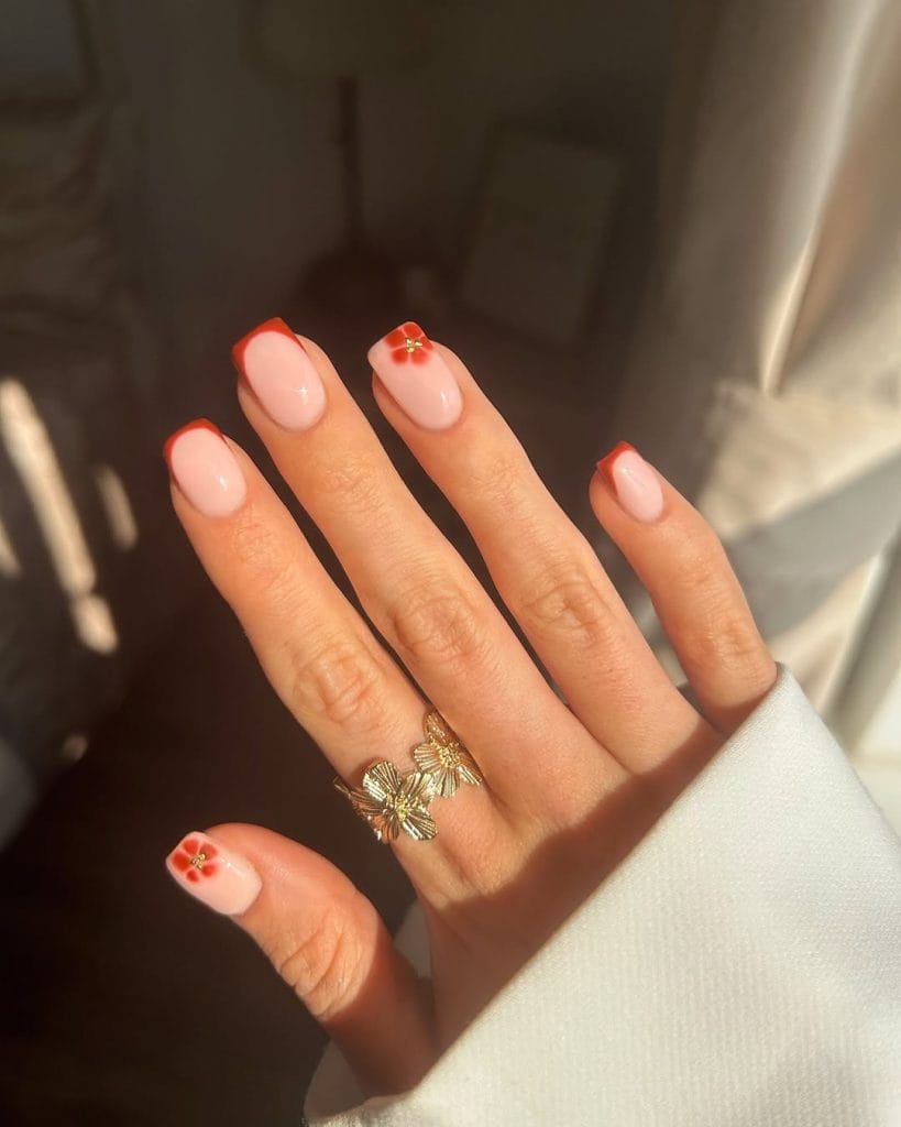 Short fall nails with pink base, orange French tips, and orange flower nail art accent
