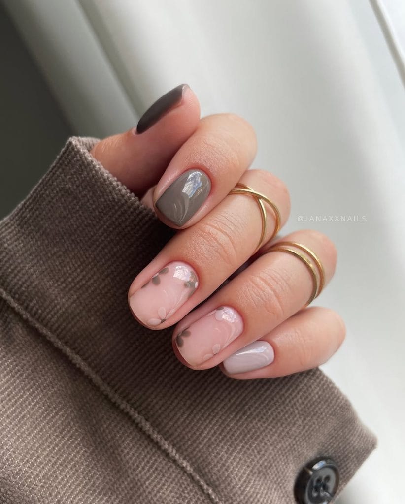 Short fall nails with two gray polish, one greige polish, and two sheer base nails with gray floral designs
