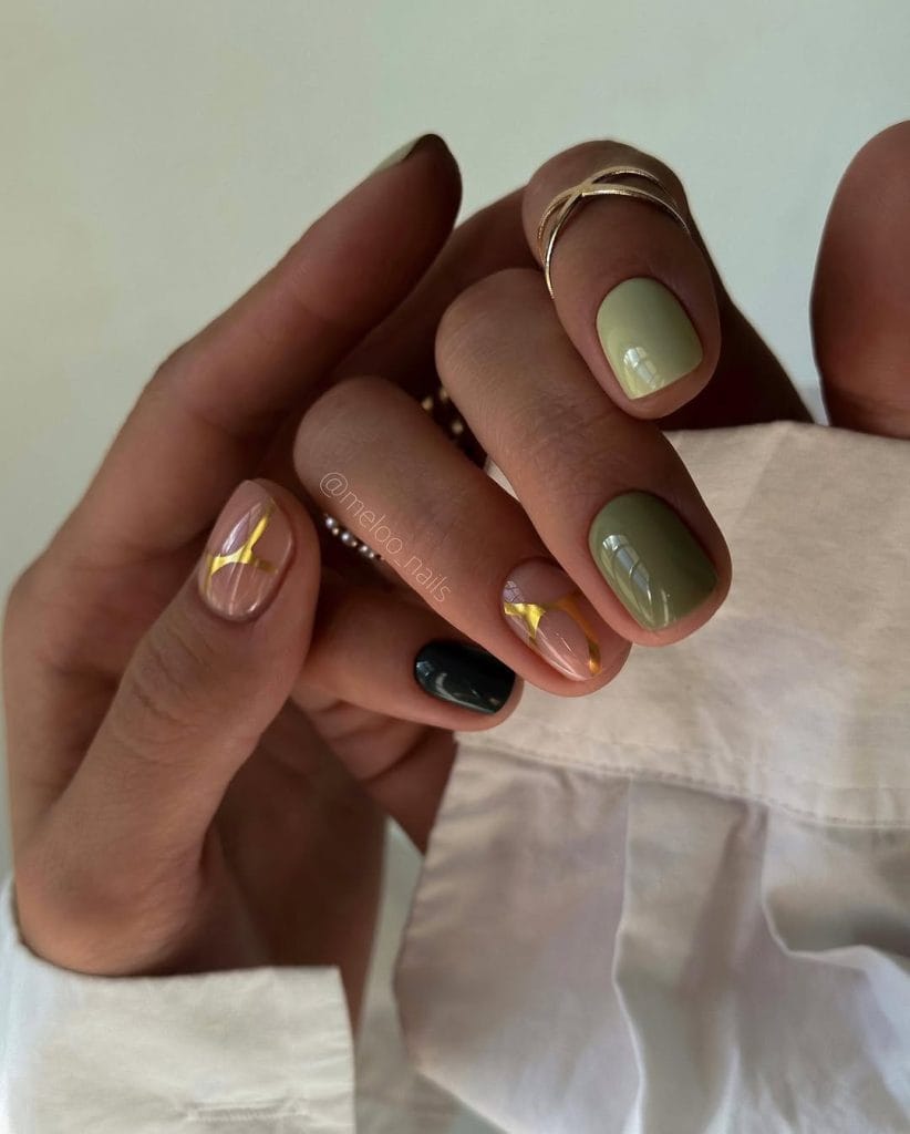 Short fall nails with mixed olive and sage green shades and sheer pink accent nail with gold foil design
