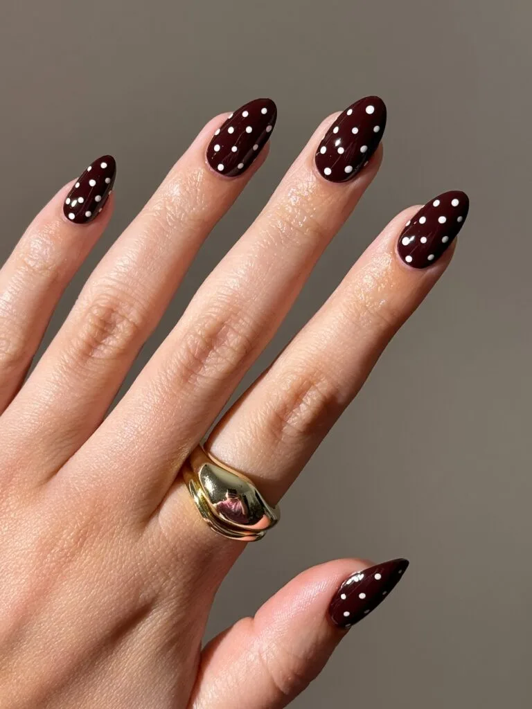 Brown fall nails with small white polka dots on glossy dark chocolate almond nails
