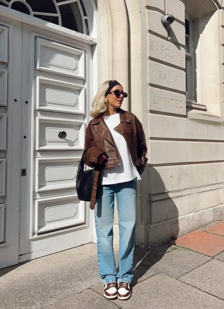 Casual fall outfit with brown leather jacket, white tee, wide-leg jeans, chunky sneakers
