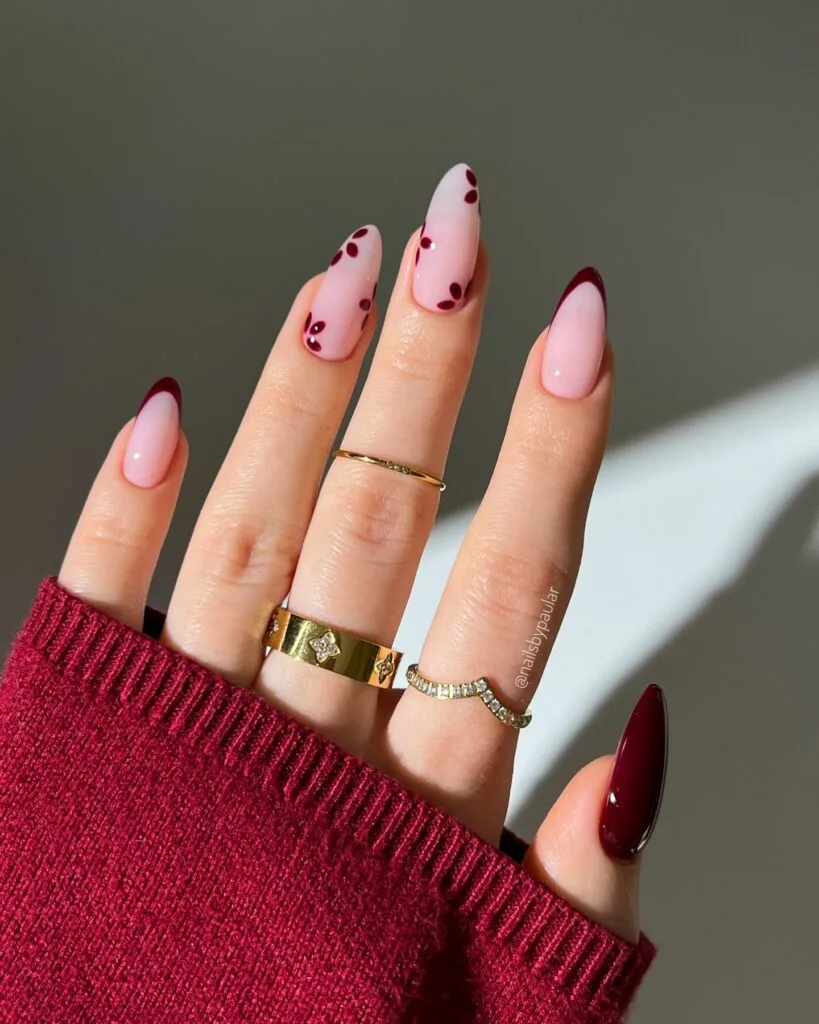 Almond autumn nails with soft pink bases, berry French tips, and small berry petal accents.